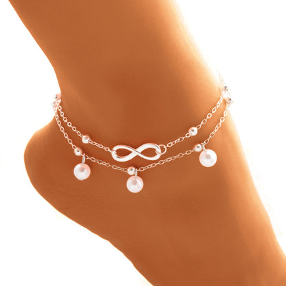Silver anklet with infinity symbol and pearls on a person's ankle against a white background