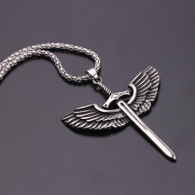 Silver pendant with wings and a sword on a chain against a dark background